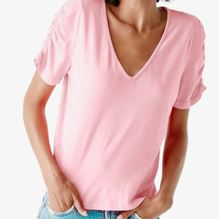 Model wearing Josie Tee in grapefruit color with V-neckline and ruched short sleeves tucked into high-rise denim.