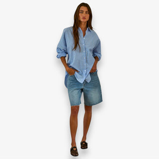 Woman wearing a blue striped shirt and denim shorts on a white background