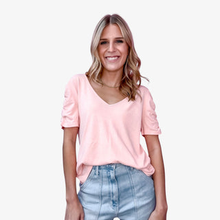 Model wearing Josie Tee in grapefruit color with V-neckline and ruched short sleeves tucked into high-rise denim.