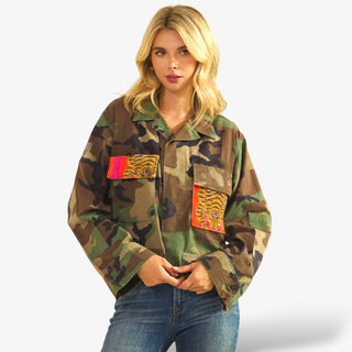 Woman wearing a camouflage jacket with colorful patches on a white background