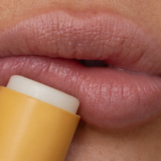 Close-up of a person applying yellow lip balm to their lips.