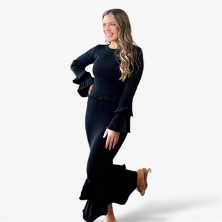 Woman wearing a black dress with ruffled sleeves and hem on a white background