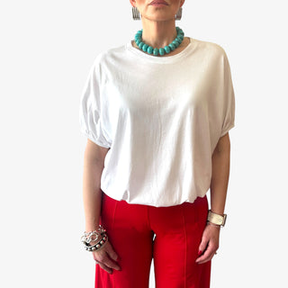 White cotton blouson blouse with elastic waist and short sleeves styled with a red pant and turquoise necklace