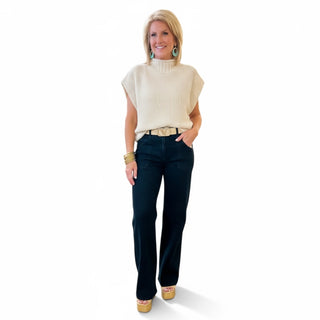 Woman wearing a cream sweater and black wide leg jeans on a white background