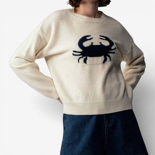 Person wearing a cream sweater with a black crab design on a white background