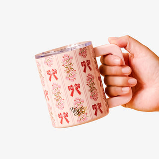 Hand holding a pink mug with floral and bow design on a white background