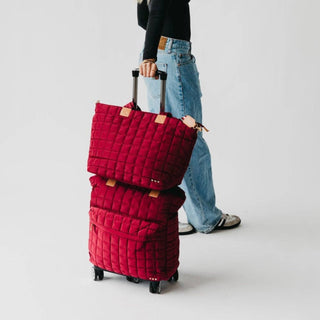 Person holding a stack of red quilted suitcases on a light gray background