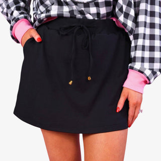 Women's black performance skort with side pockets, adjustable drawstring waist and gold-tone tips, shown in a front detail view.