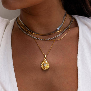 Close-up of a person wearing multiple necklaces with a gold pendant.
