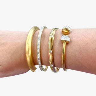 Wrist wearing multiple gold and silver bracelets on a white background