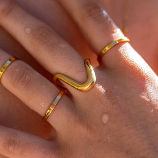Close-up of a hand wearing three gold rings on a blurred background