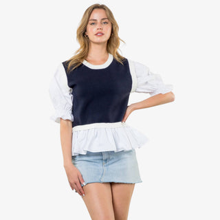Woman wearing navy mixed media peplum top with white puff sleeves and ruffle hem.