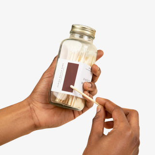 Hand holding a jar of matches with a matchstick, on a white background