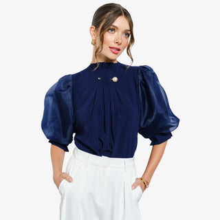 Woman wearing navy puff sleeve blouse with pleated detail and pearl accent