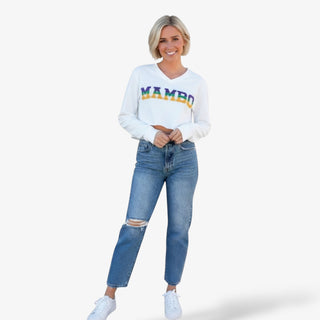 Woman wearing a white sweatshirt with Mambo in purple, green and gold and jeans on a white background