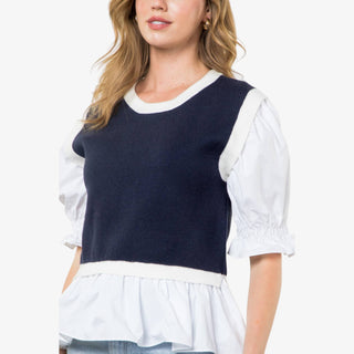 Woman wearing navy mixed media peplum top with white puff sleeves and ruffle hem.