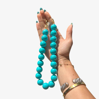 Turquoise bag charm necklace with oversized round beads and gold-tone clasps shown held outdoors in a front view.