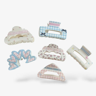 Set of six pastel hair claws in gingham, floral, and heart designs with soft pink, blue, and cream tones for a cute, feminine accessory collection.
