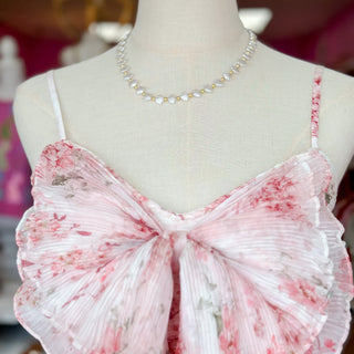 Mannequin wearing a pink and white floral dress with a blurred background and seashell necklace