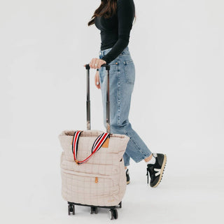 Person pulling a large beige quilted bag with a striped handle on a white background