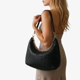 Woman holding a black woven handbag against a plain background