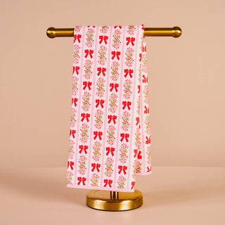 Towel with red bow pattern on a gold towel rack against a beige background