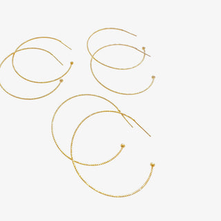 Dainty gold plated hoop earrings with thin textured design displayed on jewelry card with lace background
