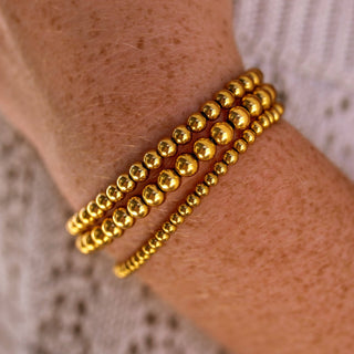 Gold beaded bracelets on a wrist with a neutral background