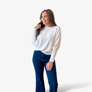Woman wearing a white sweater and blue jeans against a white background