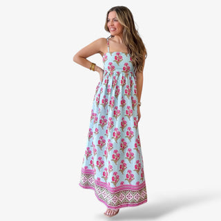 Blue floral maxi dress with pink floral print, sleeveless straps, flowy tiered skirt, and patterned border hem, styled with gold bracelets and sandals
