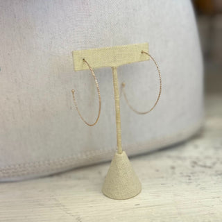 Dainty gold plated hoop earrings with thin textured design displayed on jewelry card with lace background