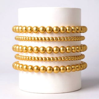 Stack of gold bracelets on a white cylindrical container against a light gray background