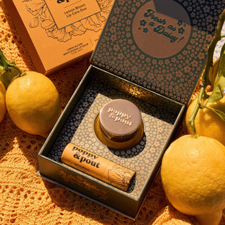 Lip balm and lip gloss set with 'peppy & pout' branding, surrounded by lemons on a textured surface.