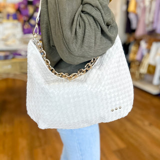 White woven shoulder bag with a chunky gold chain strap, styled with a green top and light wash jeans for a chic, elevated everyday look.