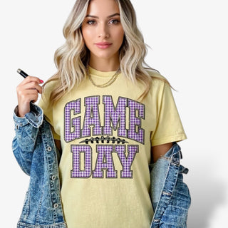 Lady wearing a yellow Game Day tshirt wit Gingham letters in purple and white.