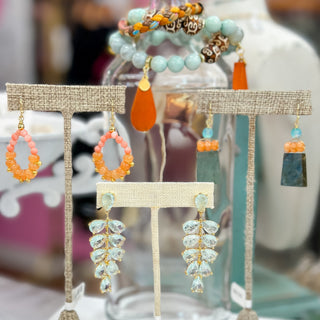 Ambre Green Statement Earrings with sparkling aqua teardrop crystals and gold accents, displayed in-store alongside colorful artisan jewelry.