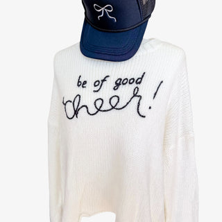 White holiday sweater with black embroidered script reading "Be of Good Cheer!"