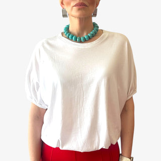 Lady wearing a white cotton blouson blouse with elastic waist and short sleeves styled with a red pant and silver earrings
