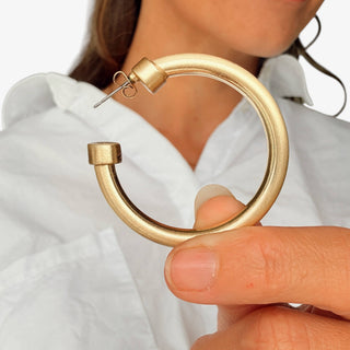 Medium Hoo Hoops brushed gold hoop earrings worn by a model, close-up view holding.