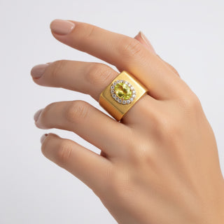 Gold ring with a green gemstone on a hand against a light gray background