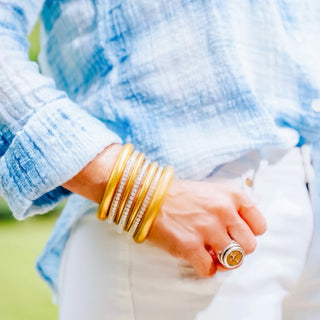 BudhaGirl All Weather Gold Bangles stacked with crystal accent bangles styled with blue textured blouse and white jeans close-up view