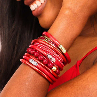 Person wearing multiple red bangles  with gold, rosegold and silver accents.