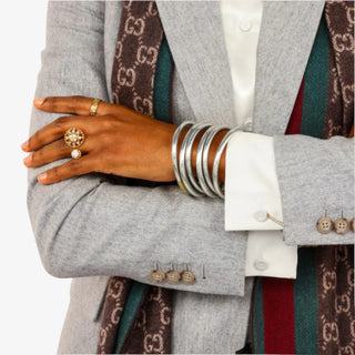 Person wearing a gray blazer with a patterned tie and silver bangles.