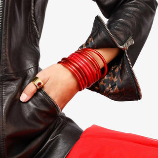 Person wearing a black leather jacket with red bangles and a gold ring.
