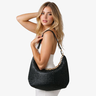 Woman holding a black woven handbag against a plain background