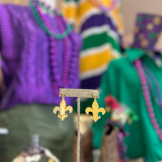 Gold fleur-de-lis earrings on a stand with colorful blurred background