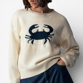 Beige sweater with a blue crab design worn by a person on a plain background