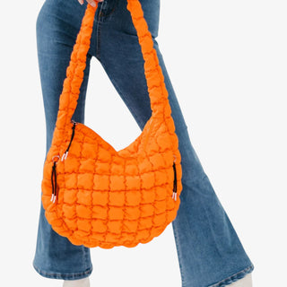 Orange quilted handbag held by a person wearing blue jeans on a white background
