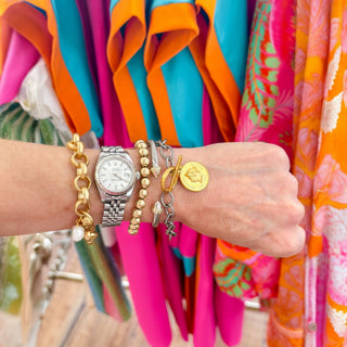 Wrist with multiple bracelets and a watch against colorful fabric background