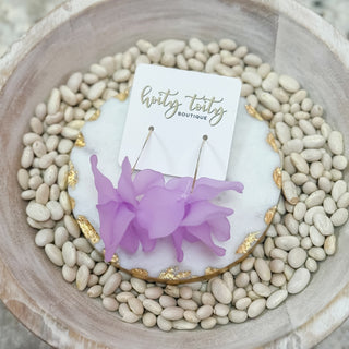 Purple floral earrings on a white card with 'hotty totty boutique' branding, placed on a bed of small stones.